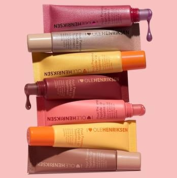 Flat lay of multiple Ole Henriksen Pout Preserve Lip Treatment tubes in assorted shades on a pink background.